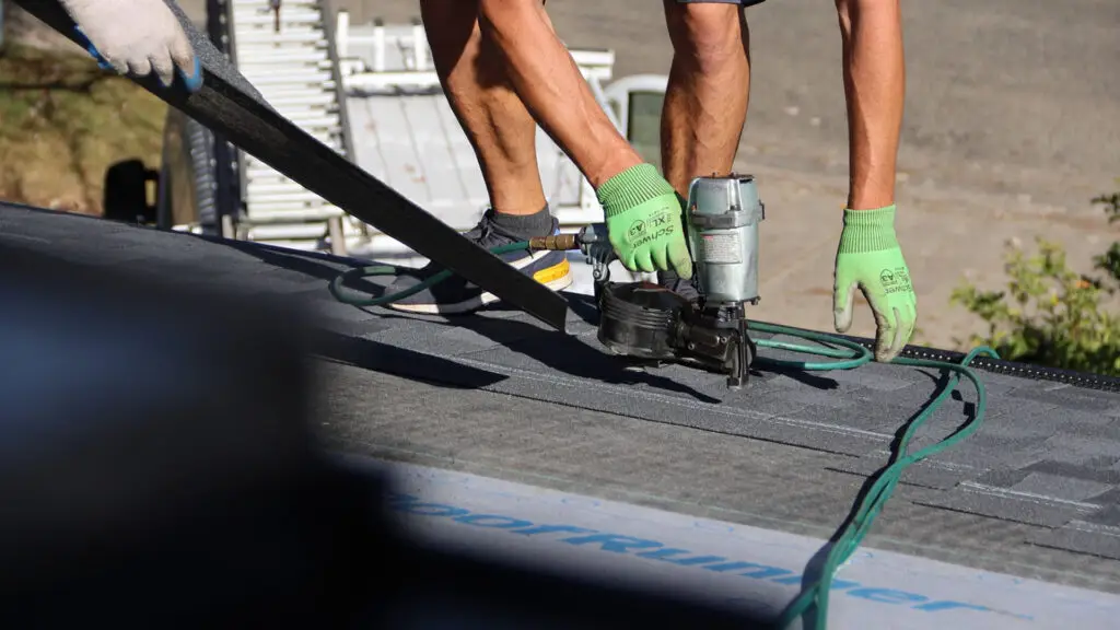 Roofer using nail gun to install asphalt shingles on residential roof in Almont, MI.
