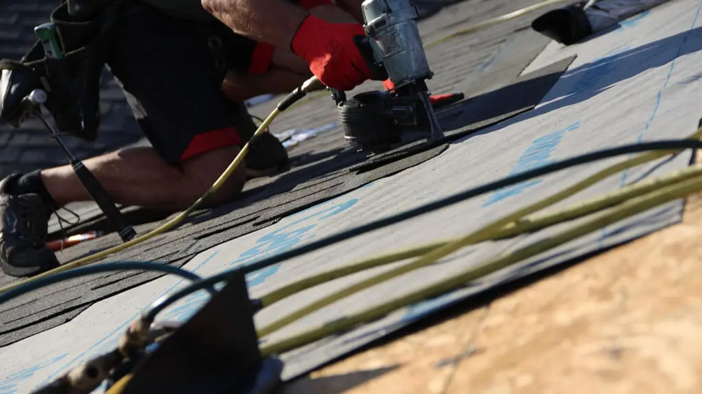 roofer using nail gun to secure asphalt shingles on roof in Fenton, MI
