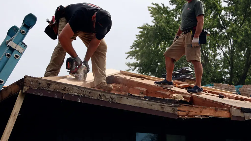 Roofers using a circular saw to cut replacement wood for rafter repairs during a roof replacement in Southfield, MI.