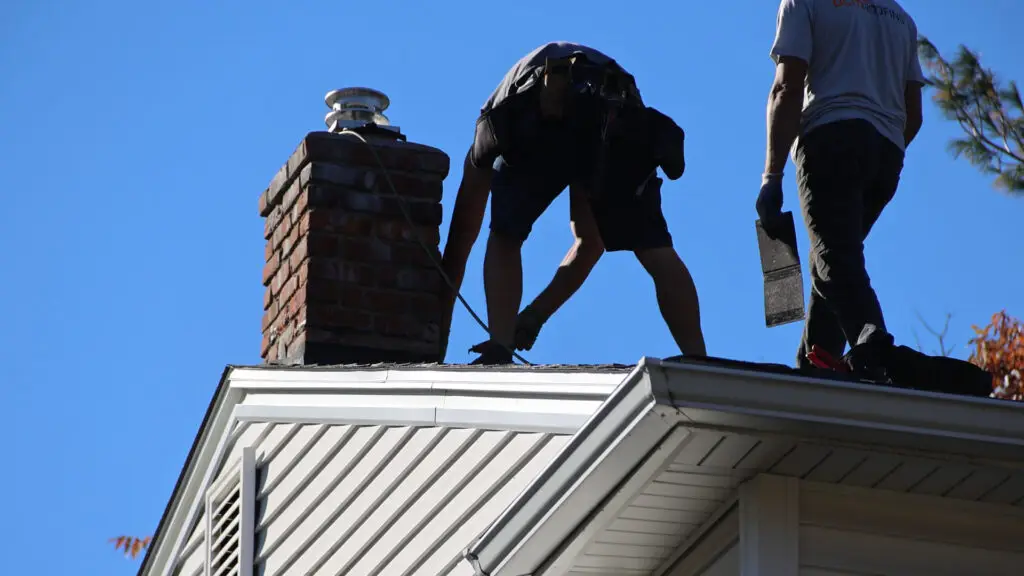Roofing crew installing asphalt shingles around a chimney during roof replacement in Metamora, MI.