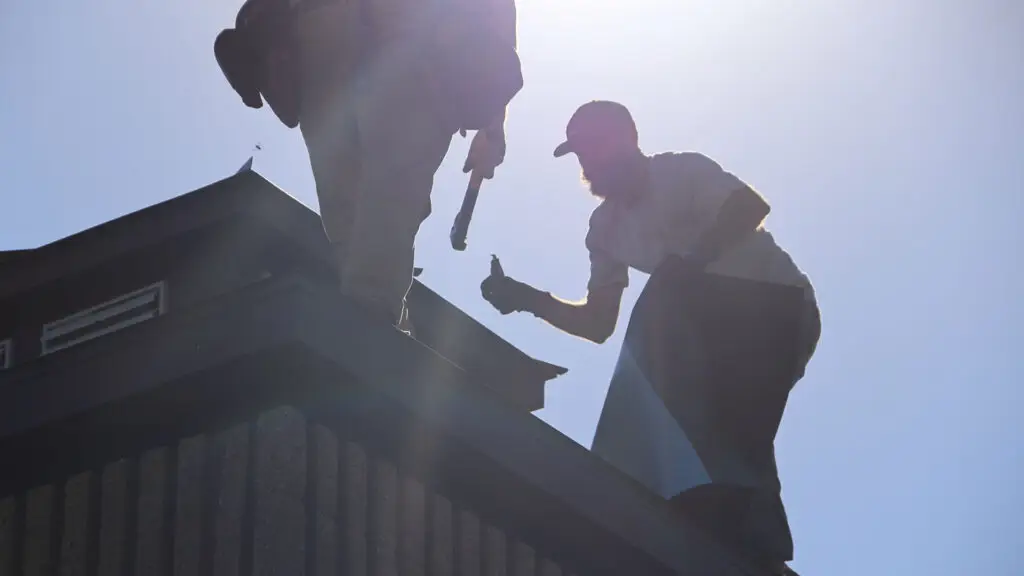 Roofing crew installing synthetic underlayment at the roof edge during a roof replacement in Goodrich, MI.