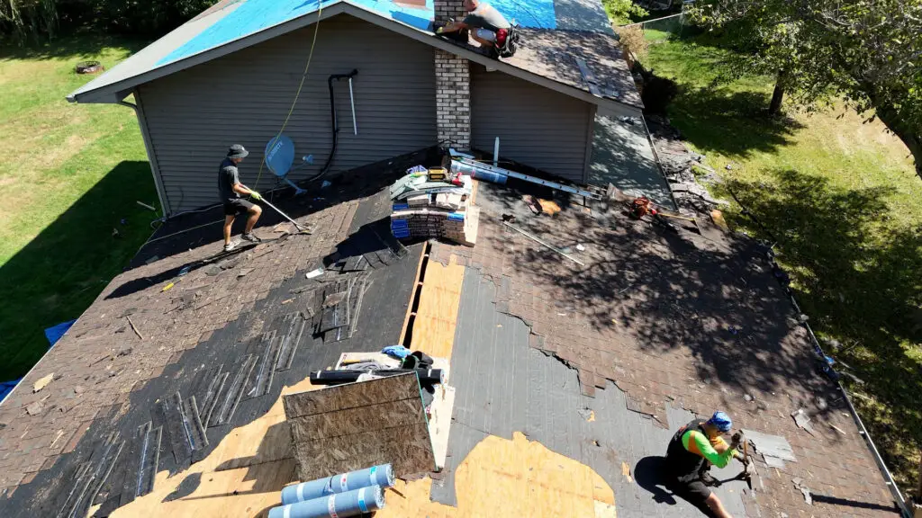 Roofing crew removing old shingles and underlayment during residential roof replacement in West Bloomfield, MI.