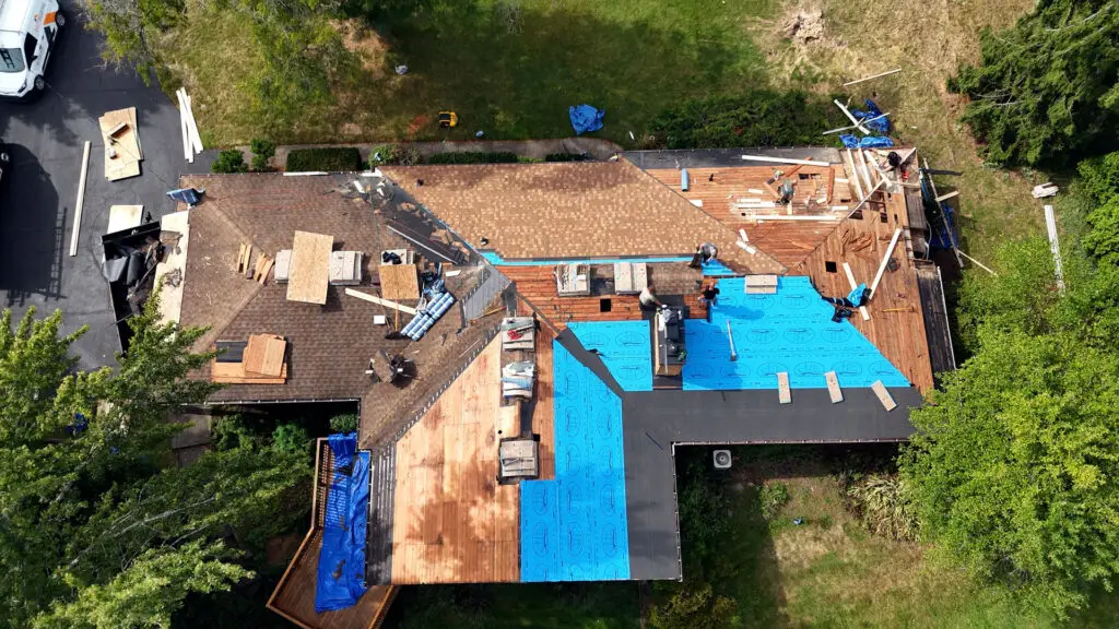 Roofing crew repairing damaged rafters and installing synthetic underlayment during roof replacement in Lapeer, MI.