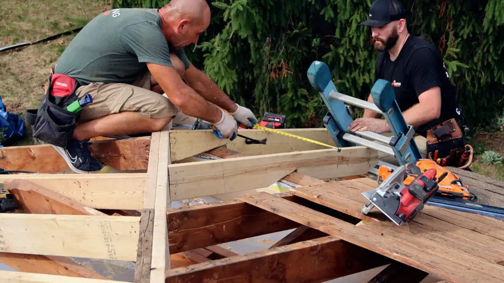 Roofing crew repairing damaged roof framing and decking during roof replacement in Ortonville, MI.