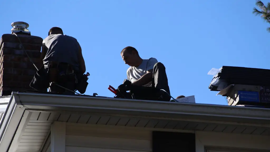Roofing crew securing step flashing around chimney during roof replacement in Farmington, MI.