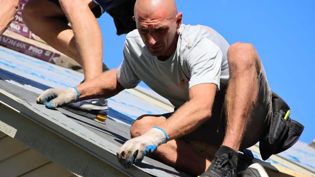 Two roofers positioning starter shingles on a rake edge in Troy, MI.
