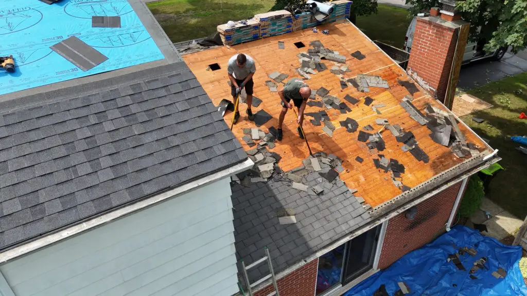 Two roofers removing old asphalt shingles during a residential roof replacement in Waterford, MI.