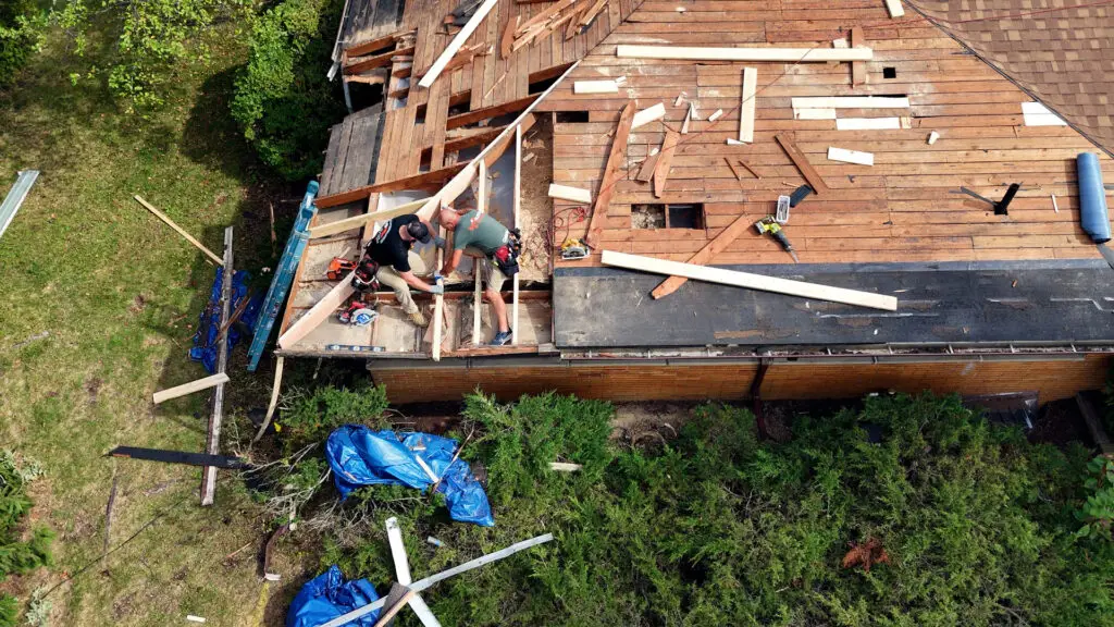 Two roofers repairing damaged rafters and decking during a roof repair in Clarkston, MI.